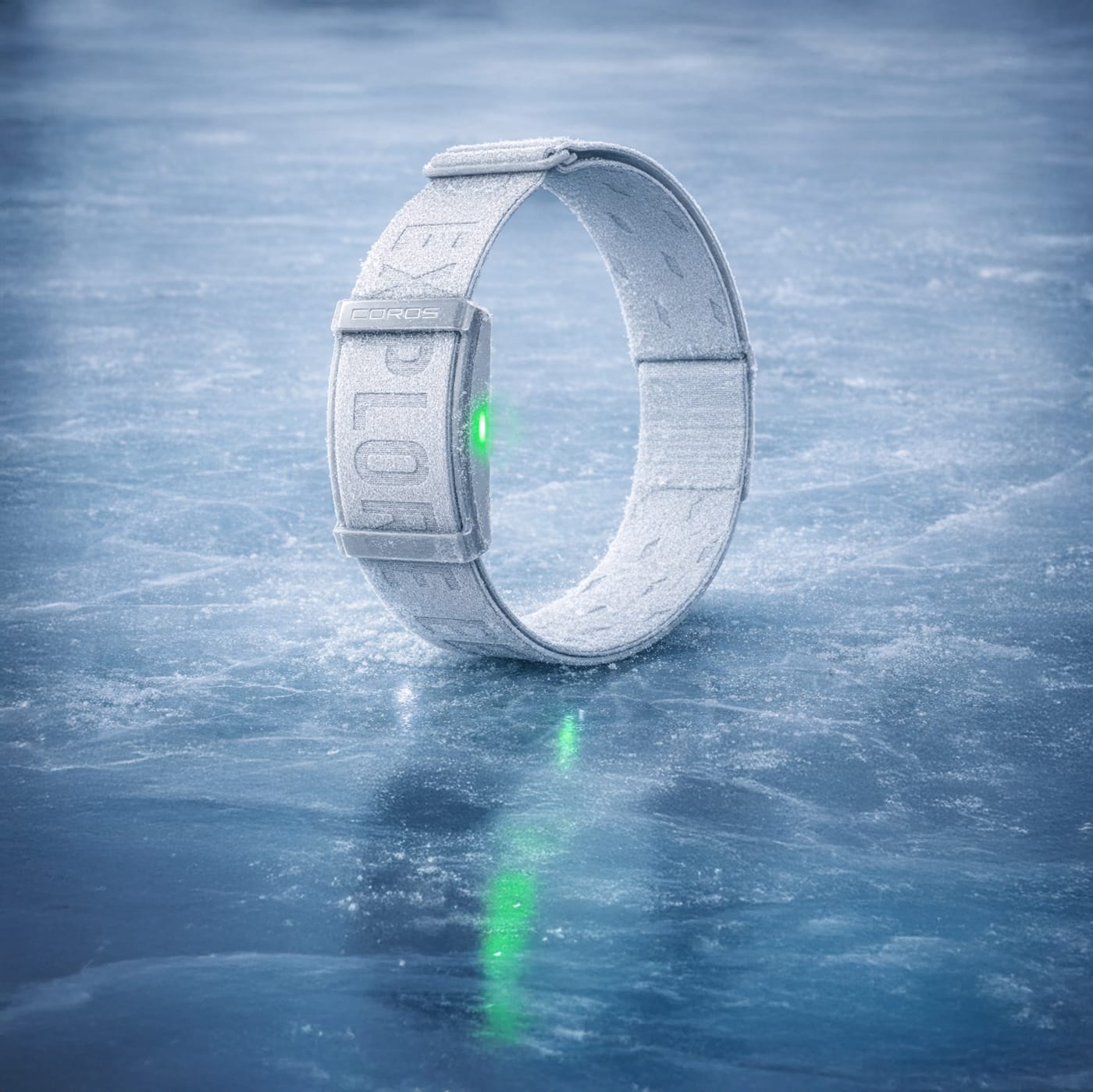 COROS heart rate monitor band standing upright on a frozen ice surface, covered in frost with a green LED glowing, set against a cold blue winter background