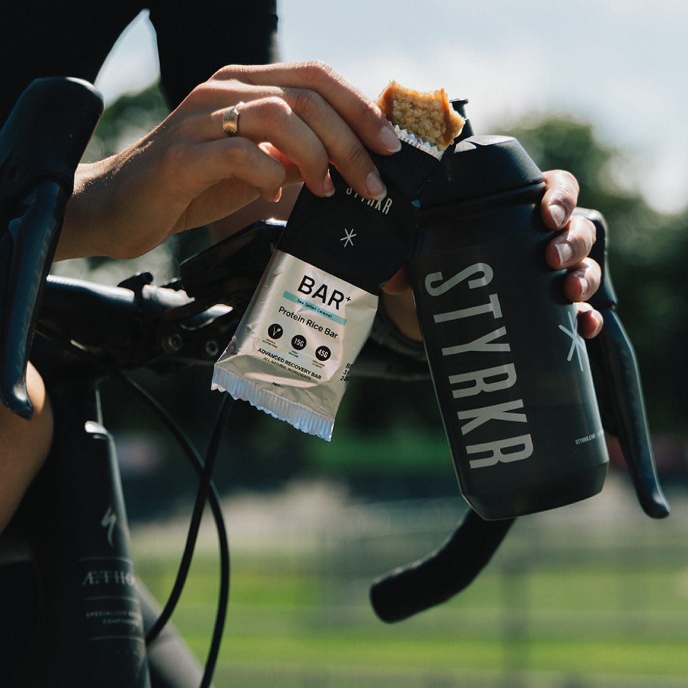 STYRKR energy bar held next to STYRKR cycling bottle during a ride