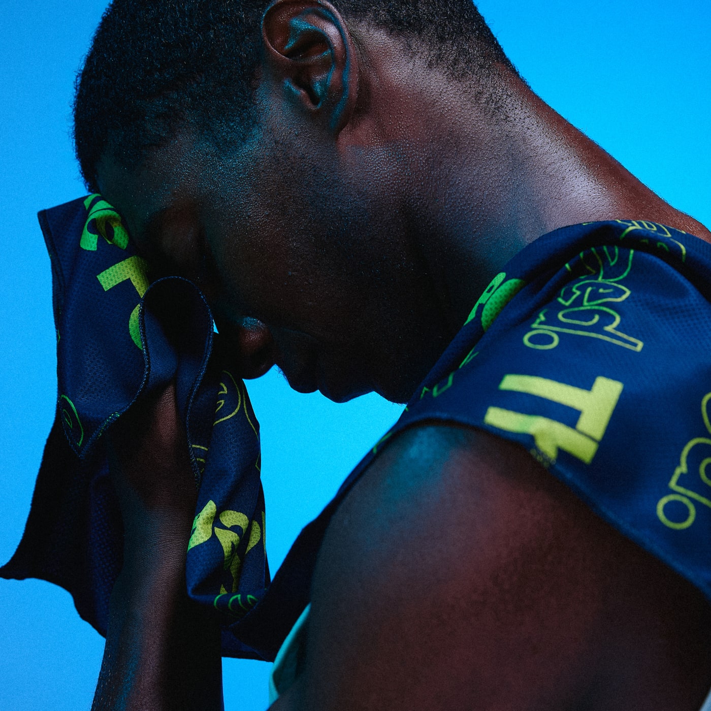 Athlete cooling down with a navy and neon yellow The Feed towel, pressing it to his face after an intense workout, set against a bold blue background.