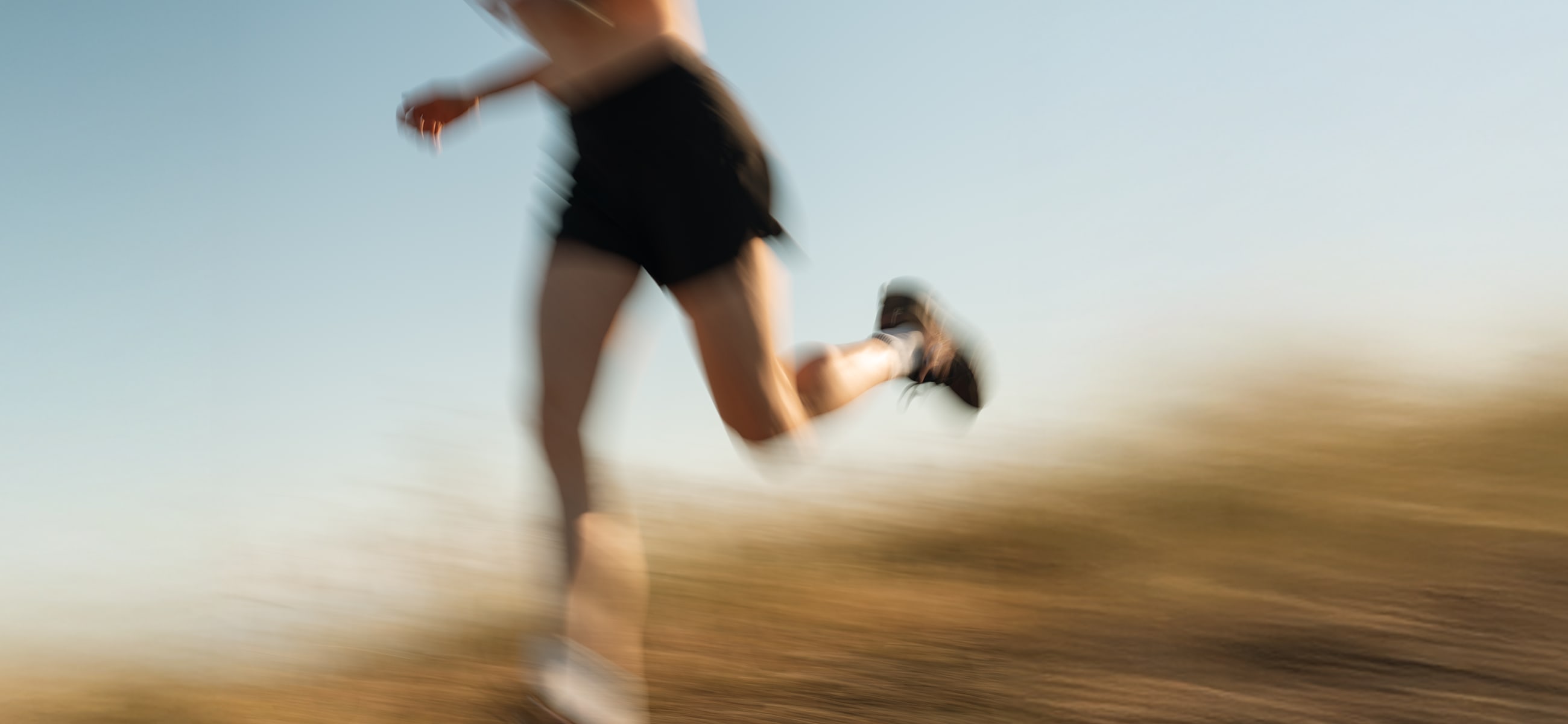 Pro triathlete Chelsea Sodaro running on a trail at sunset, captured in dynamic motion blur under a clear blue sky.