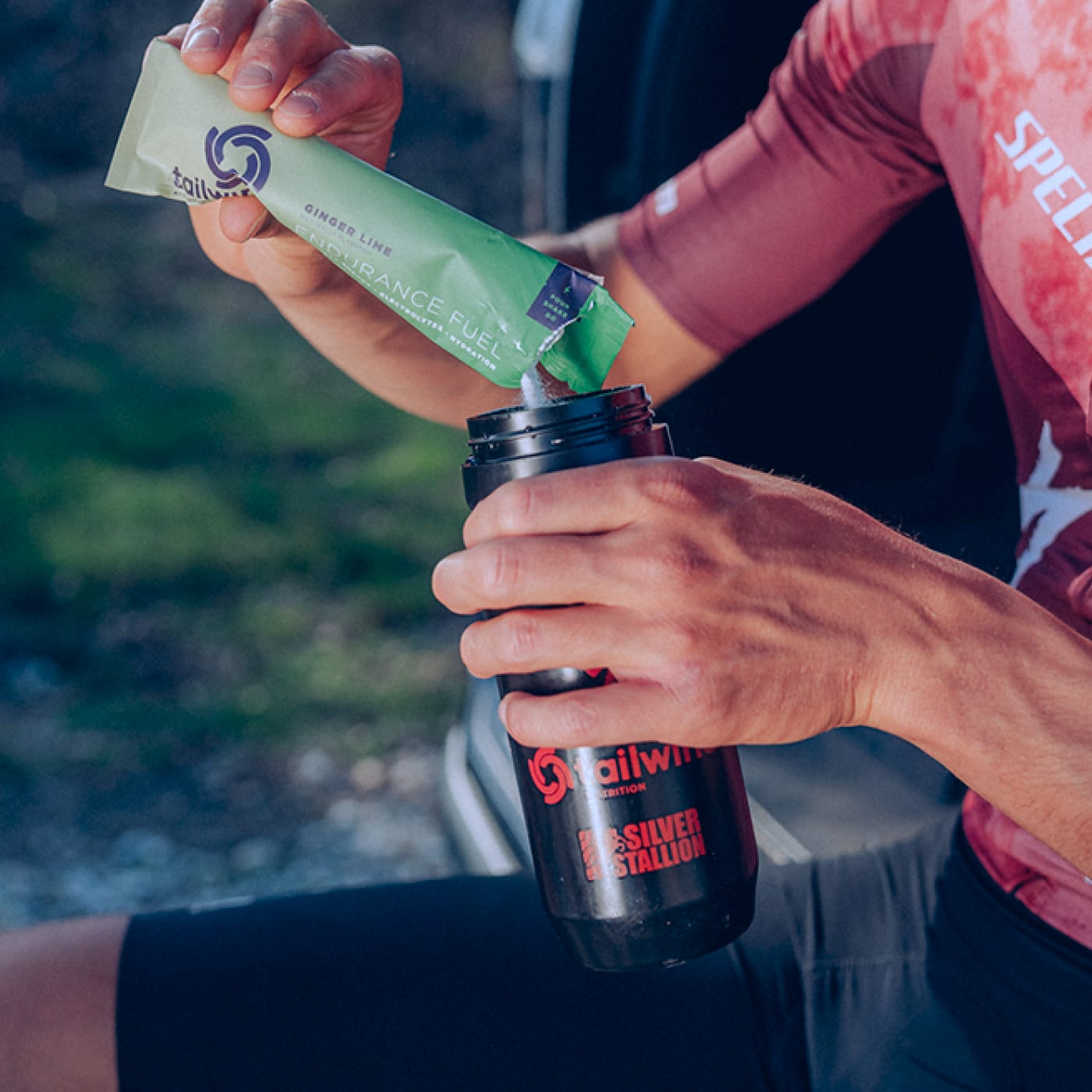 Trail athlete pouring Tailwind Nutrition Ginger Lime Endurance Fuel into a black water bottle before training, highlighting easy-to-mix hydration for sustained energy and electrolyte replenishment.