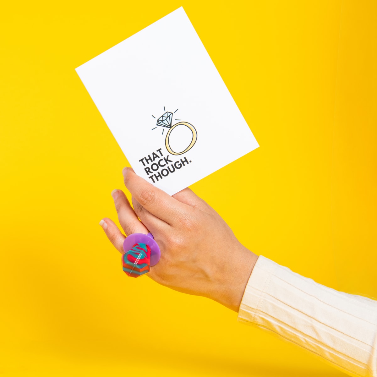 Woman wearing a ring pop holding a card that says 'That rock though'.