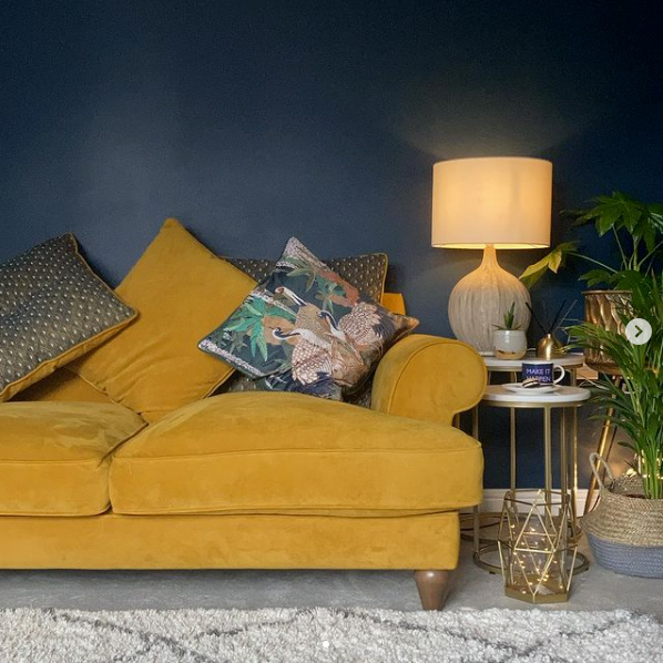 Mustard velvet sofa against a dark blue wall