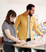 2 designers stood around a cutting table in a studio reviewing texture palettes