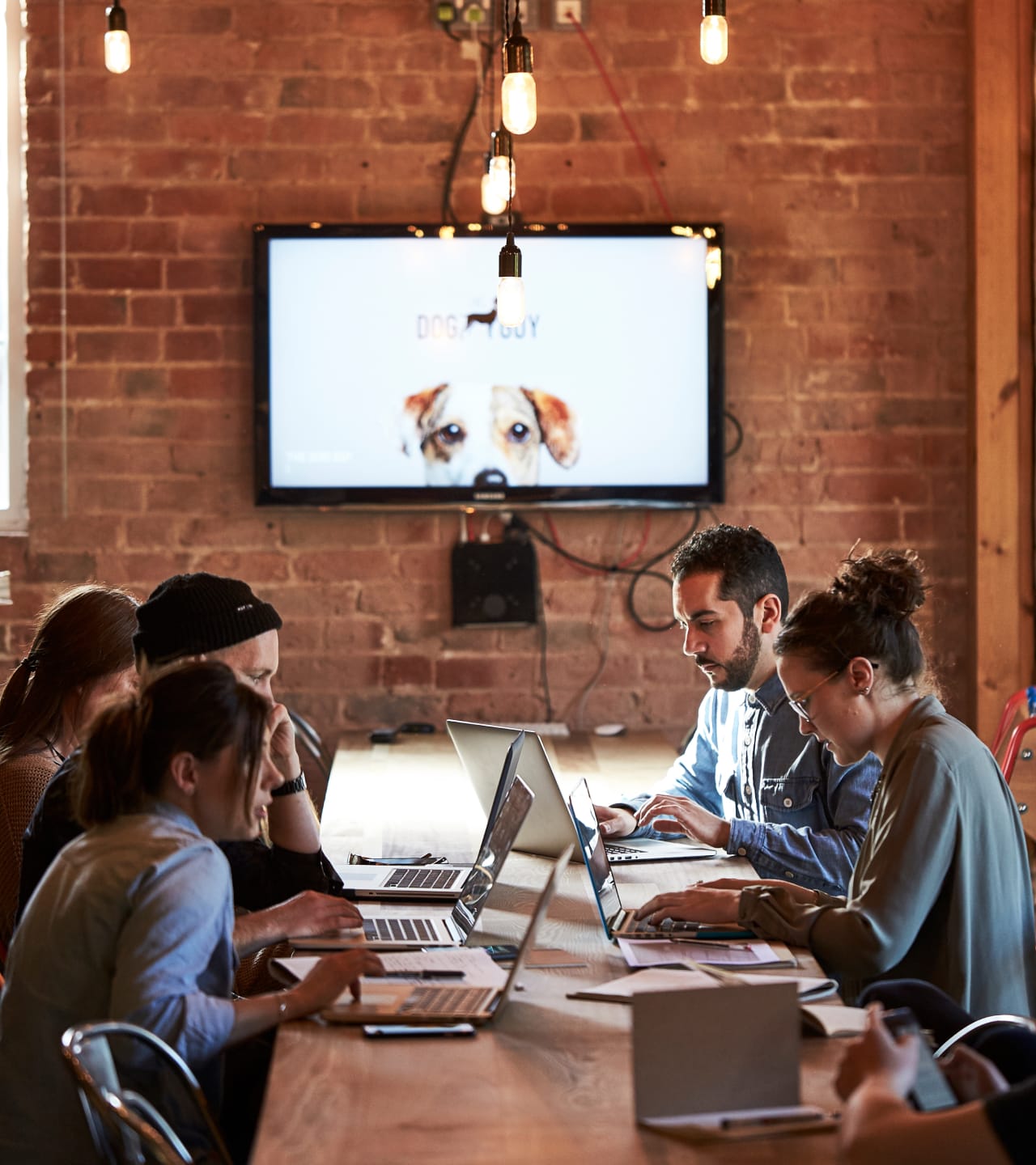 <p>A varied group of individuals sat at a large desk with their laptops.</p>
