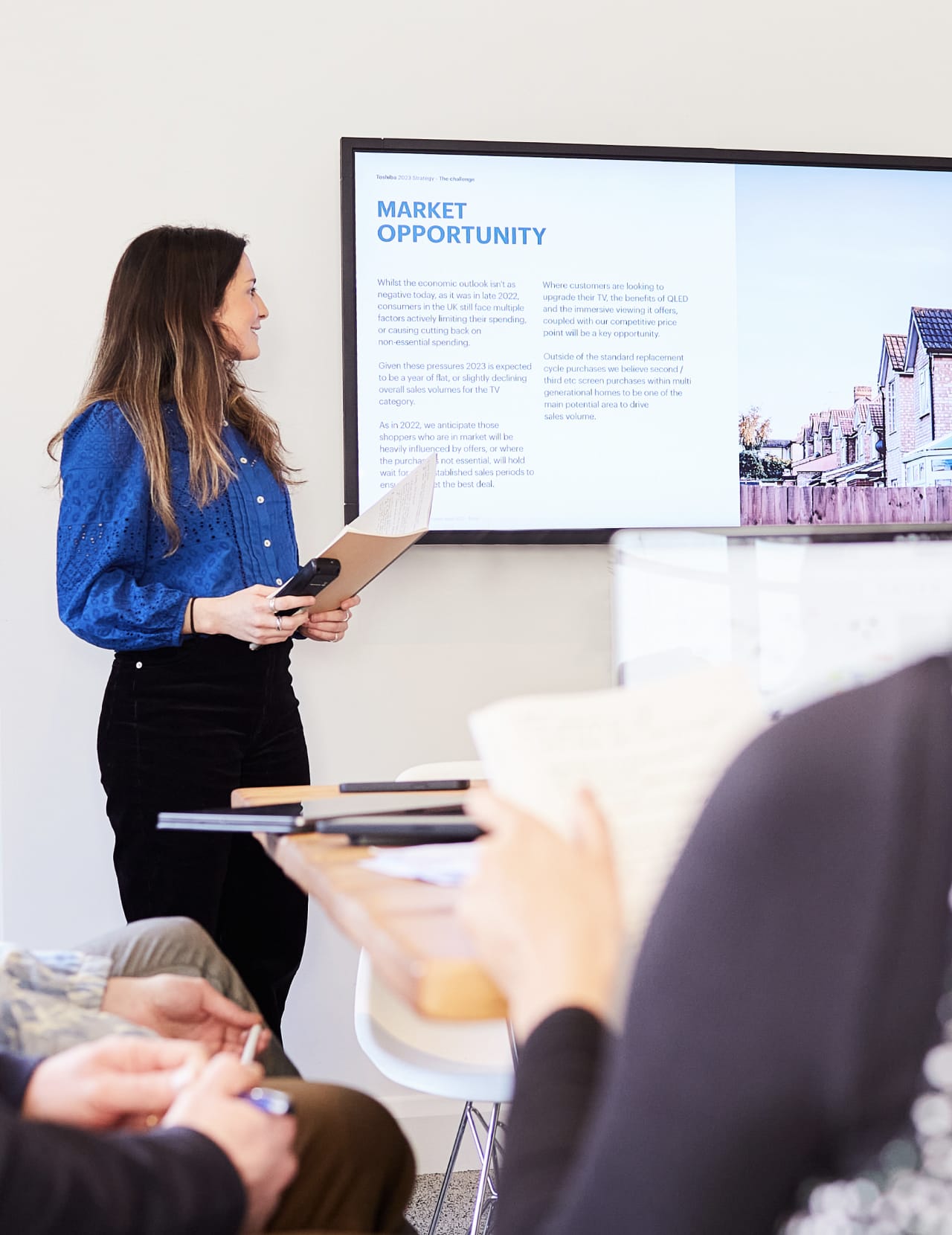 Women stood infront of a large TV presenting research insights and market opportunities