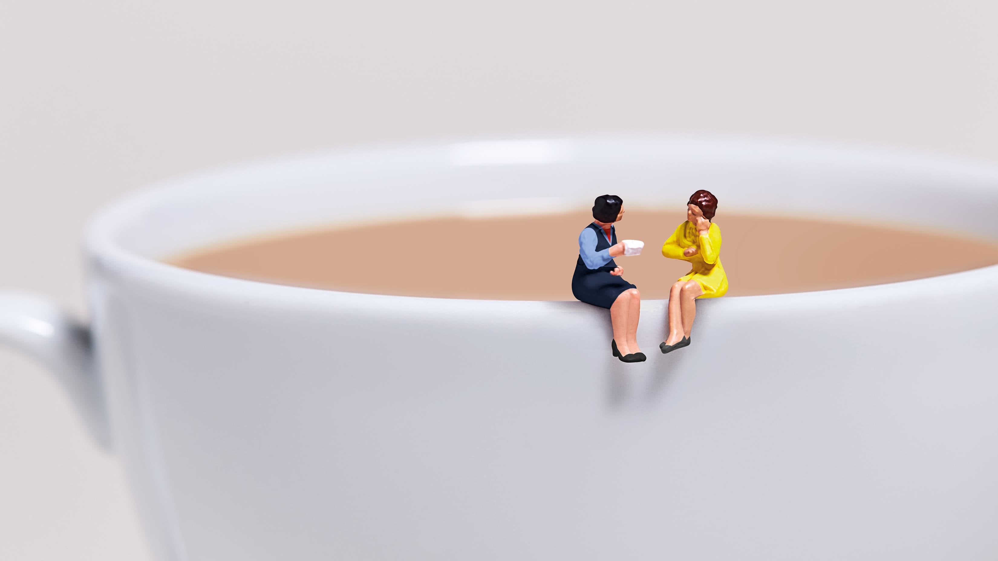 2 toy ladies sitting on the side of a cup of tea