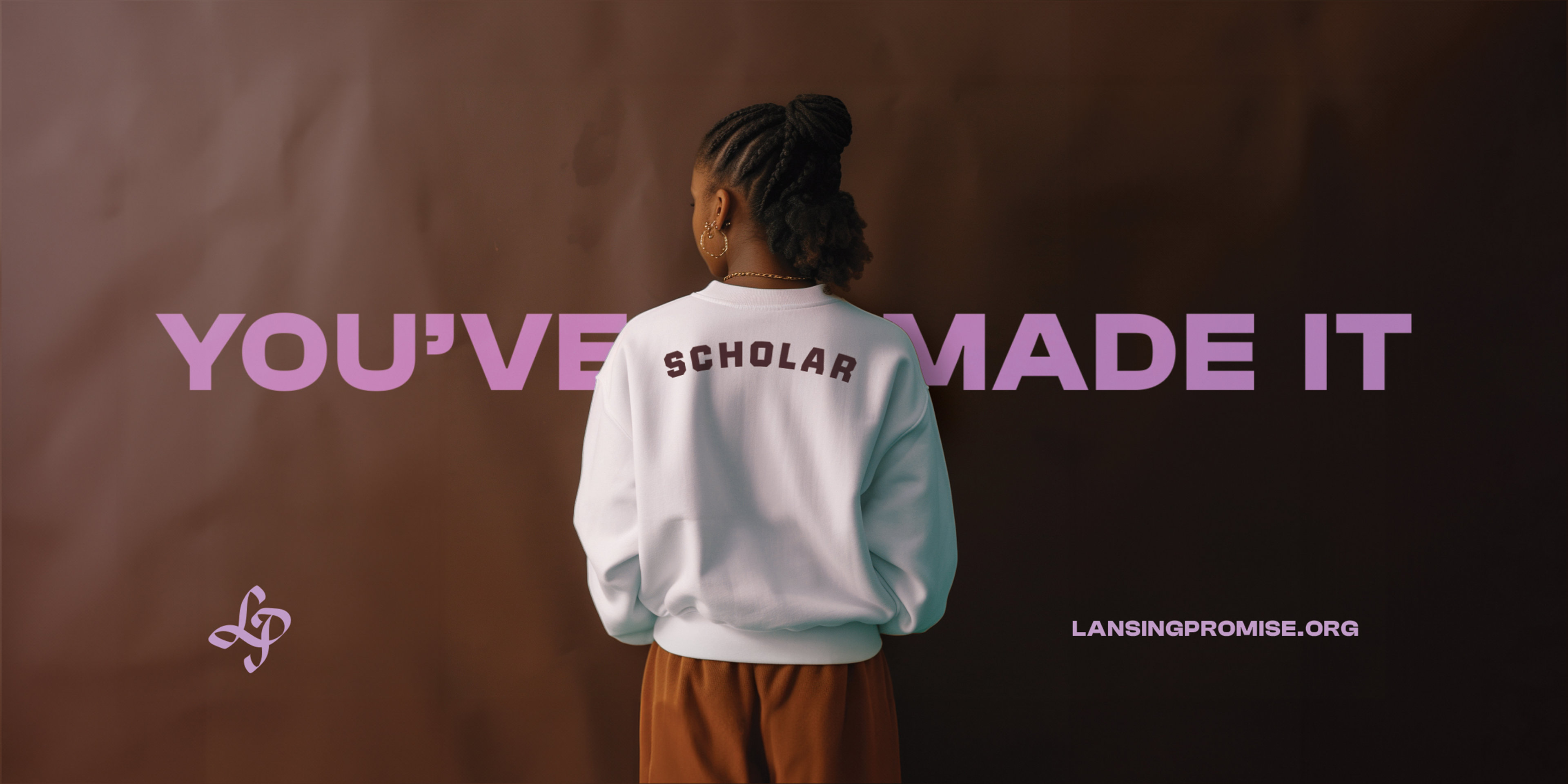 There is a rich brown paper backdrop upon which the words YOU'VE MADE IT are boldly set in light purple, a young black scholar stands confidently in the foreground with their back to the us with the word SCHOLAR embroidered across their shoulders