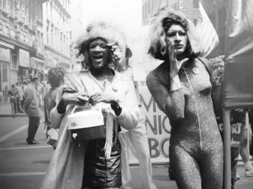 Marsha P. Johnson and another activist during a demonstration, symbolizing the visible and pioneering figures in early LGBTQ+ rights movements. Photo by Netflix. Marsha P. Johnson and another activist during a demonstration, symbolizing the visible and pioneering figures in early LGBTQ+ rights movements. Photo by Netflix.