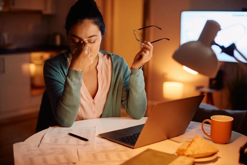 A young woman experiencing workplace stress sits thoughtfully at her desk surrounded by work essentials, illustrating the mental overload common among Millennials and Gen Z. A young woman experiencing workplace stress sits thoughtfully at her desk surrounded by work essentials, illustrating the mental overload common among Millennials and Gen Z.