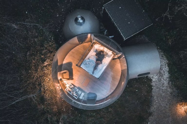 A transparent bubble dome set in a forest clearing with a cozy bedroom inside, ideal for unique Airbnb stays and immersive nature experiences. Photo by FinnLough.