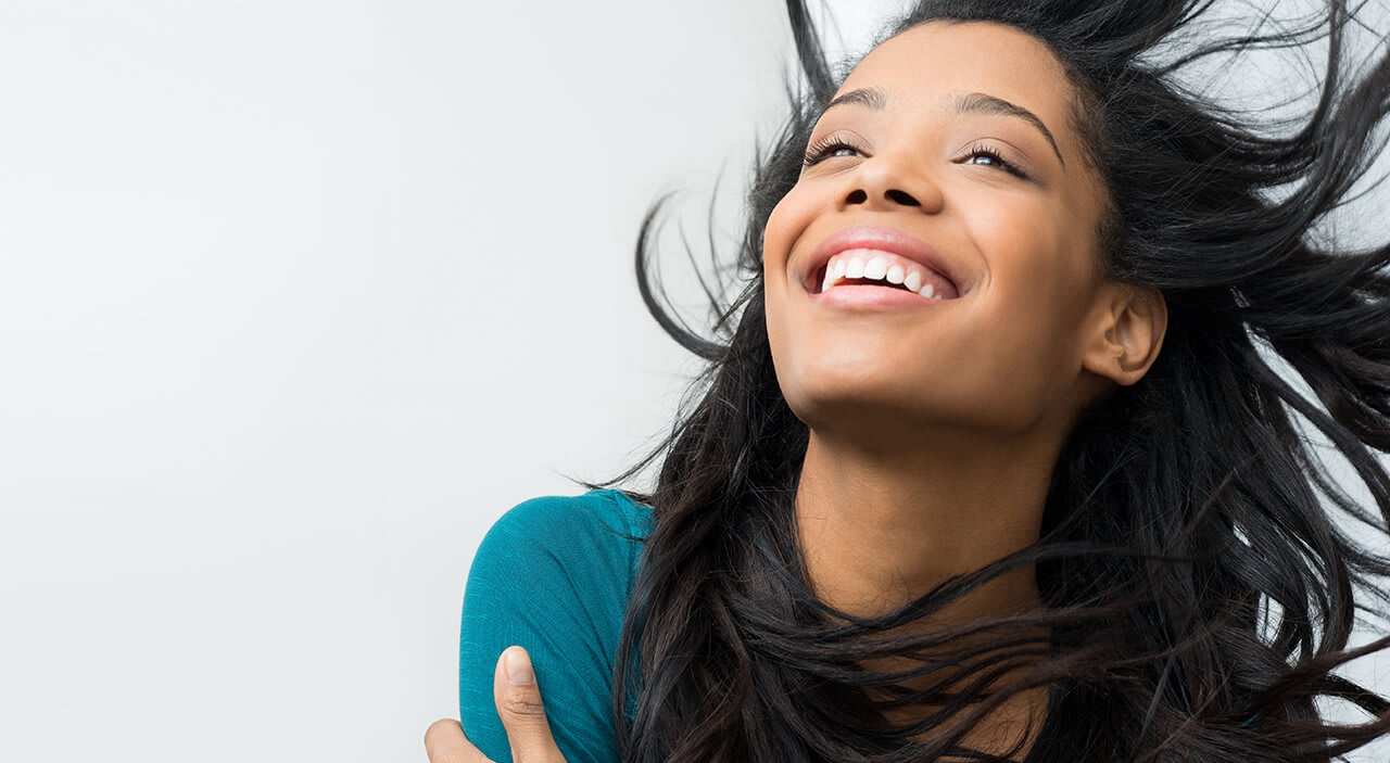 Woman with head tilted back and hair blowing in the wind laughing.