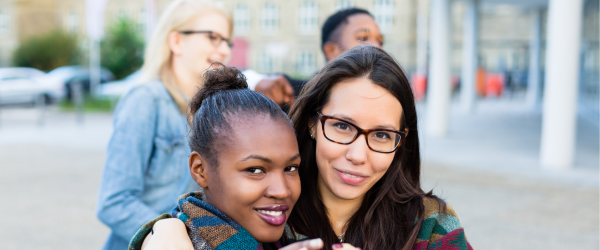 Two women smiling and holding up their hands to make a heart.