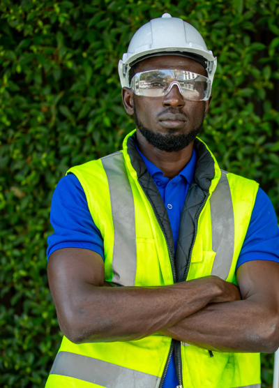 Man in hardhat and goggles standing in front of a solar panel and green background.