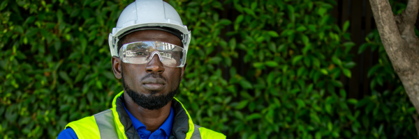 Man in hardhat and goggles standing in front of a solar panel and green background.