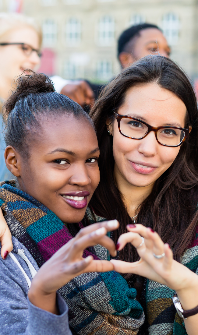 Two women smiling and holding up their hands to make a heart.