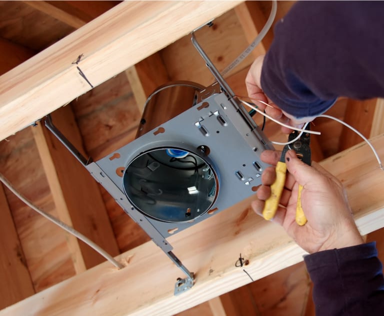 Hands using tool to repair recessed can light in ceiling