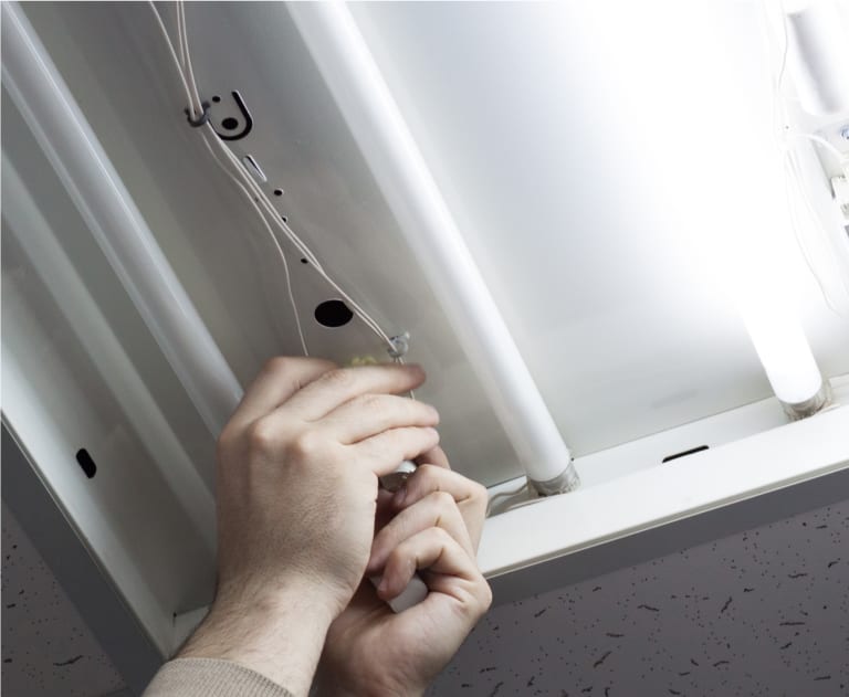 Hands repairing light bulbs or ballasts in a fixture