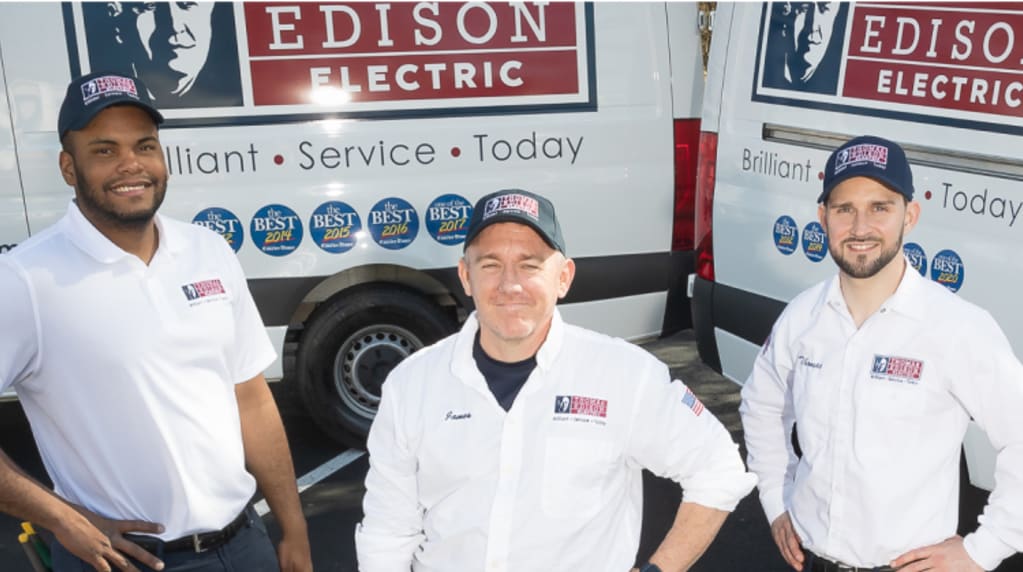 Three Thomas Edison Electric technicians stand with their work trucks