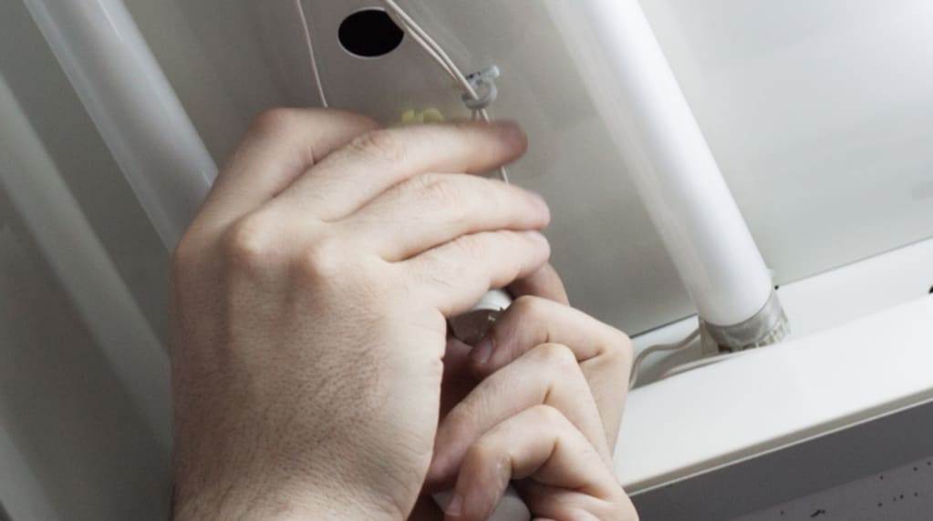 Hands repairing light bulbs or ballasts in a fixture