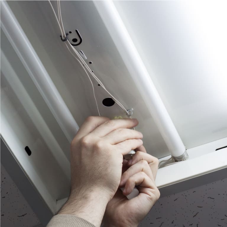 Hands repairing light bulbs or ballasts in a fixture