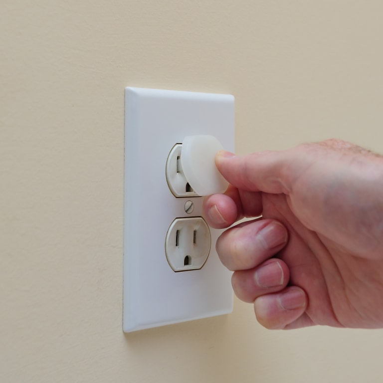 An outlet with a man inserting a child safety outlet cover into a socket