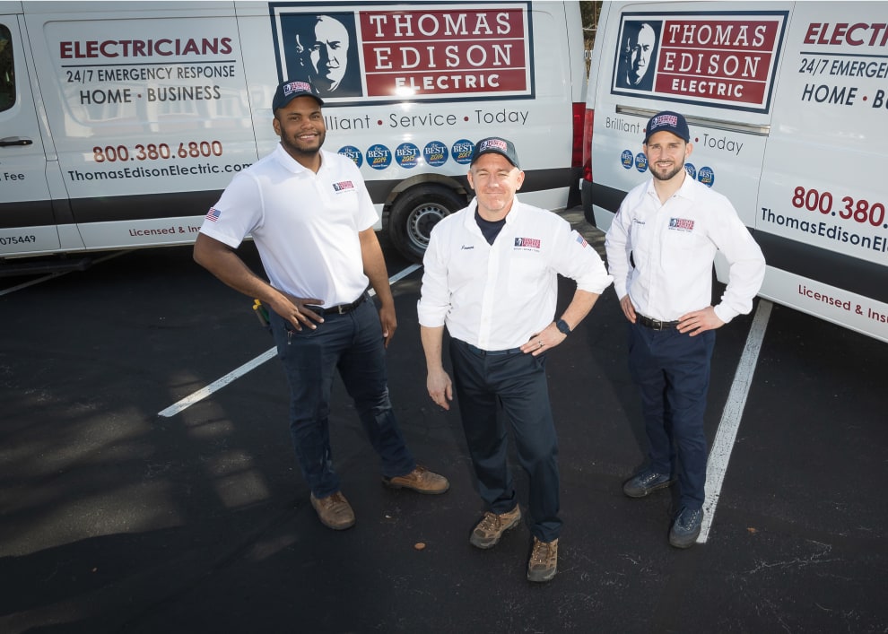 Three Thomas Edison Electric technicians stand with their work trucks