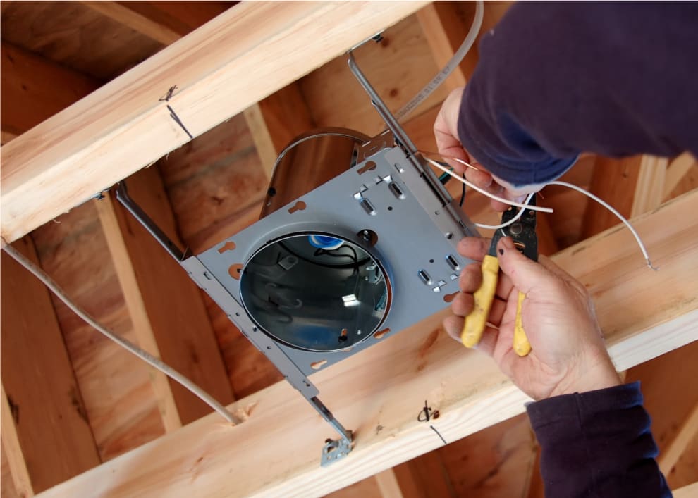 Hands using tool to repair recessed can light in ceiling