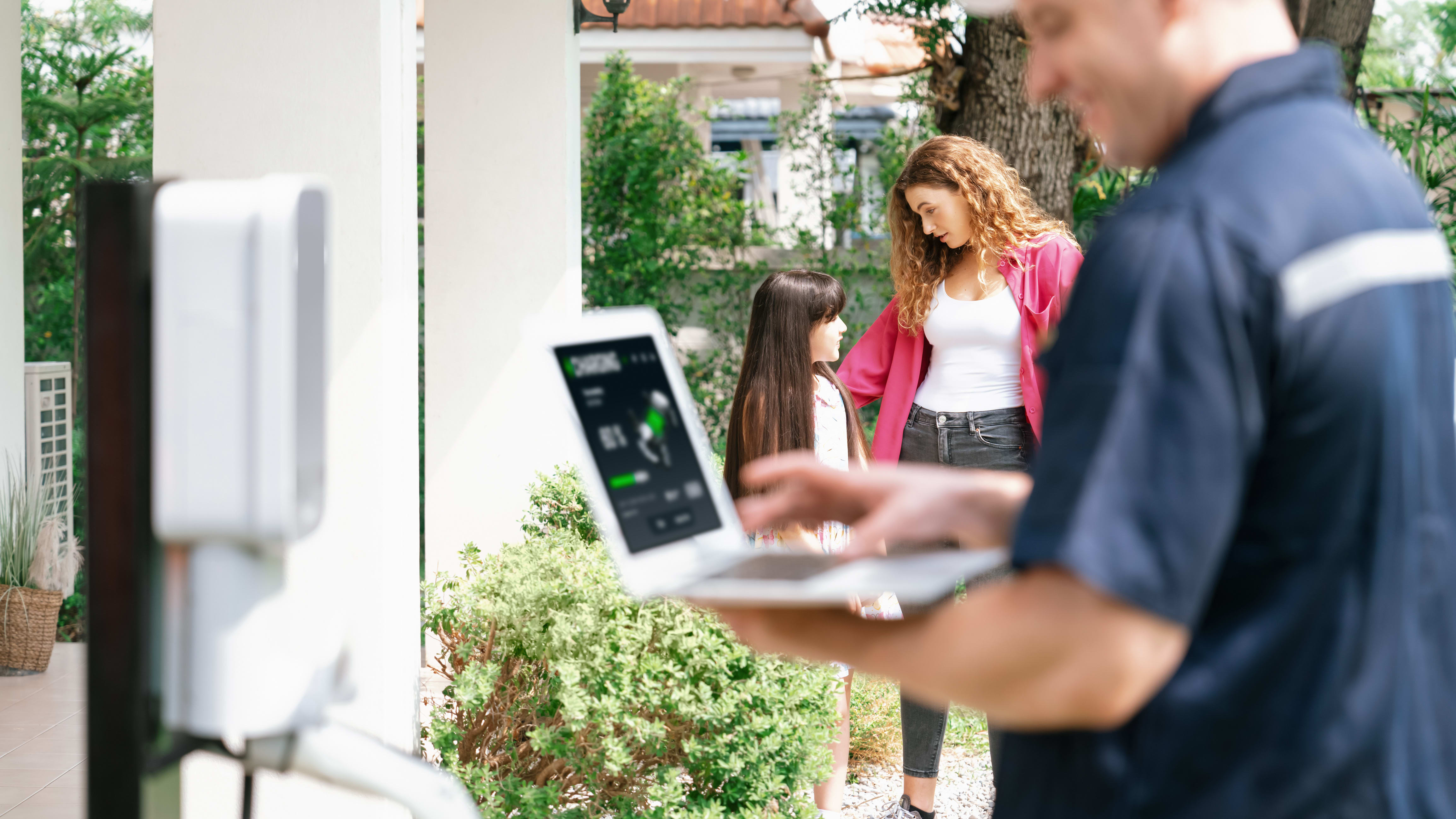 Woman and girl standing near technician doing EV charger repairs
