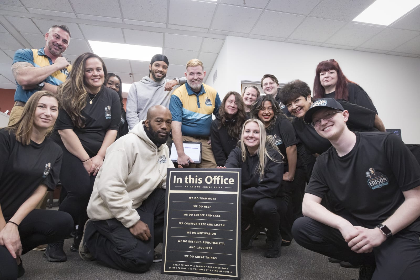 The Thomas Edison Electric team gathered around a sign listing the office rules, starting with We do teamwork