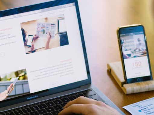 Person developing a website on a laptop, with the same site open on a mobile device on the table beside them.
