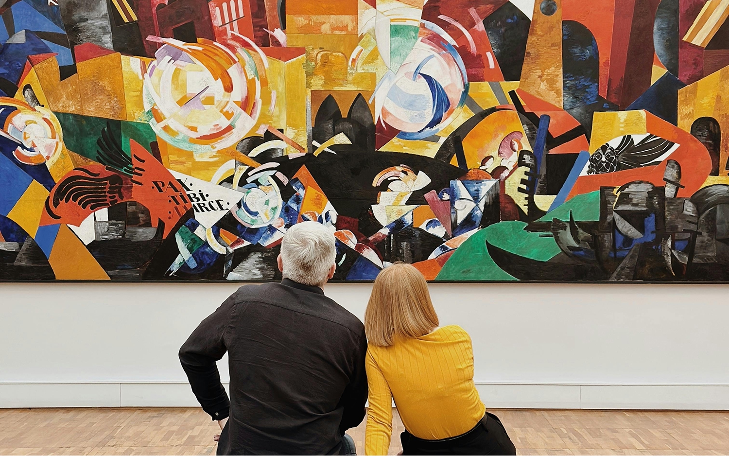 Man and woman sitting on a bench in front of a painting