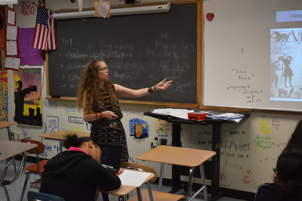 Teacher standing at whiteboard talking to the class of students