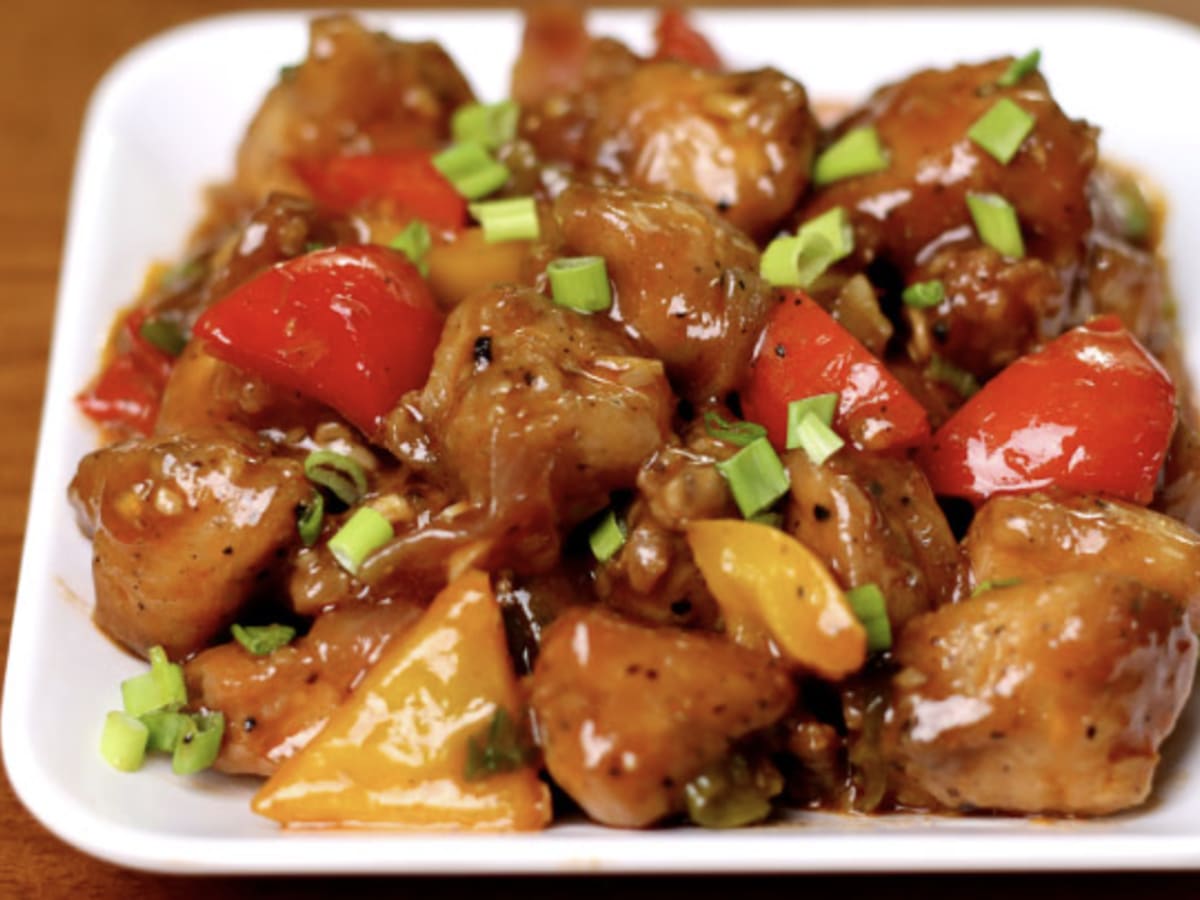 Chilli Chicken with green peppers and spring onion on a black platter