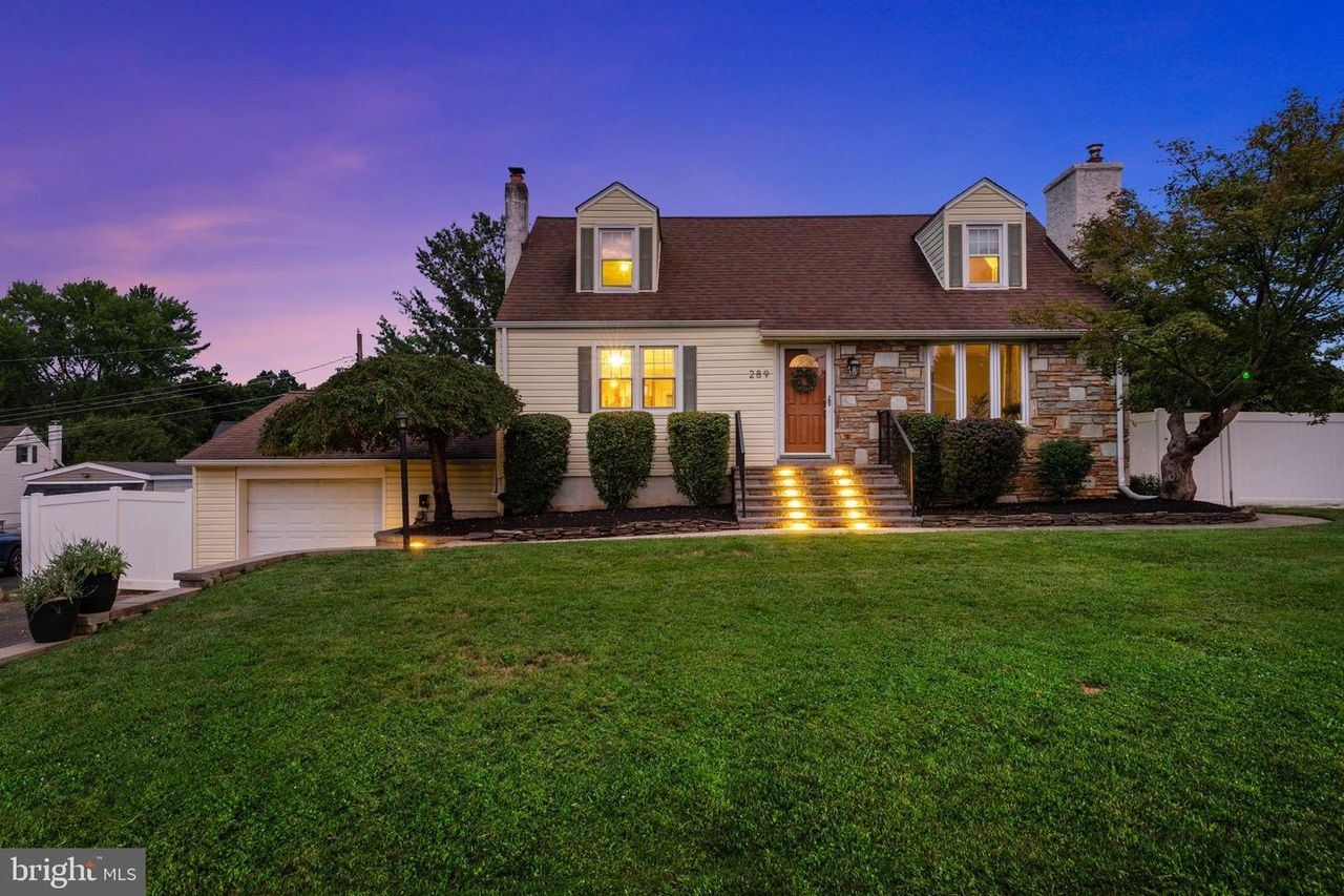 A Cape Cod home in Langhorne with lit front steps and a stone-trimmed entrance