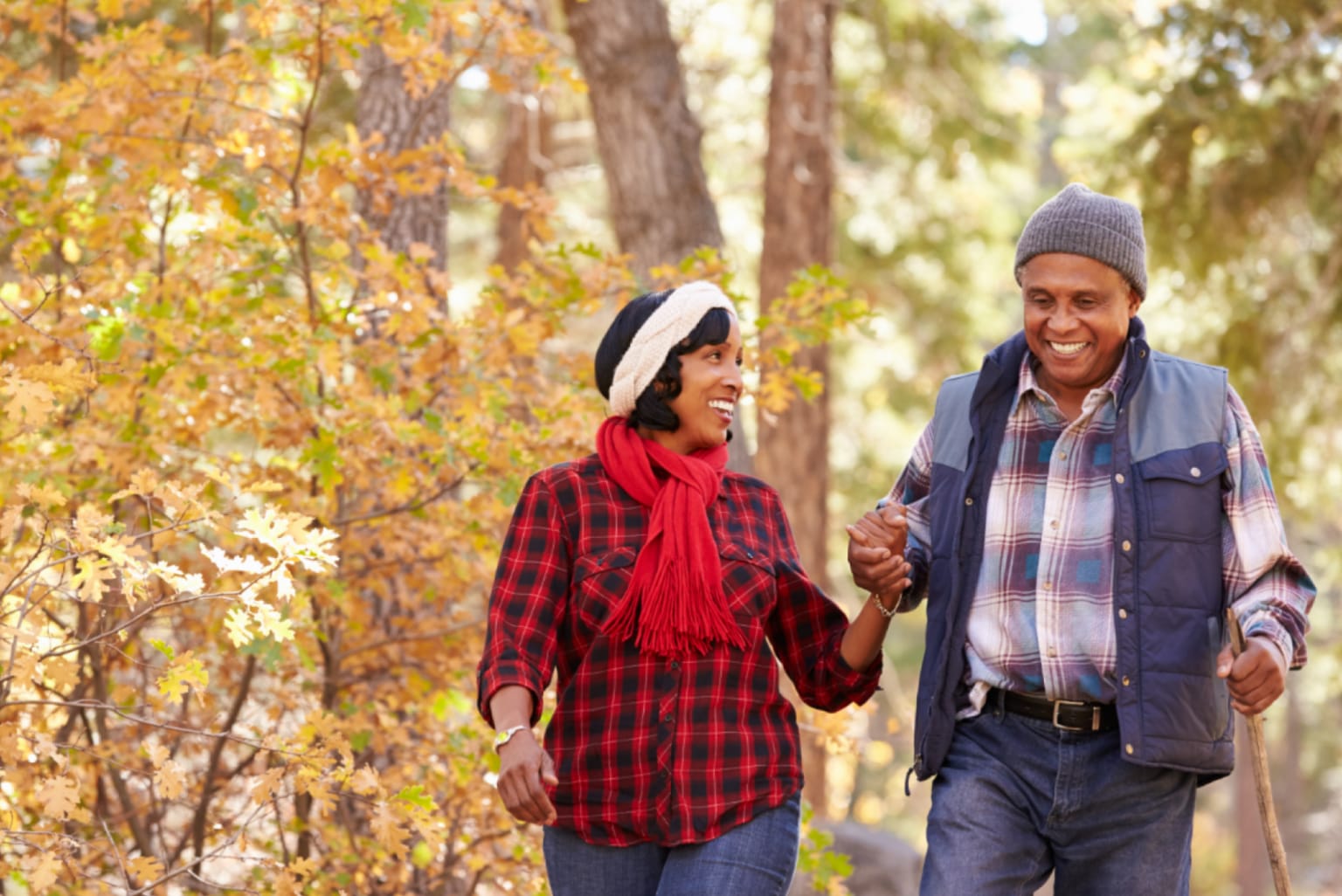 A happy man and woman walk through the Fall foliage holding hands