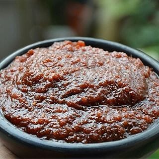 A bowl of dark Ghanaian shito with a serving spoon