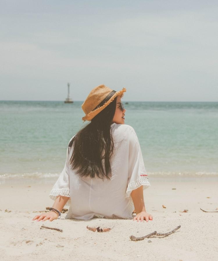 A woman sitting on the beach wearing a hat.