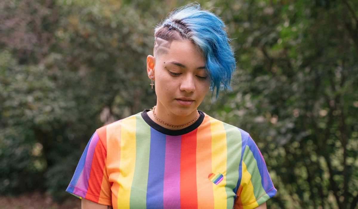 A woman with blue hair wearing a rainbow striped t - shirt.