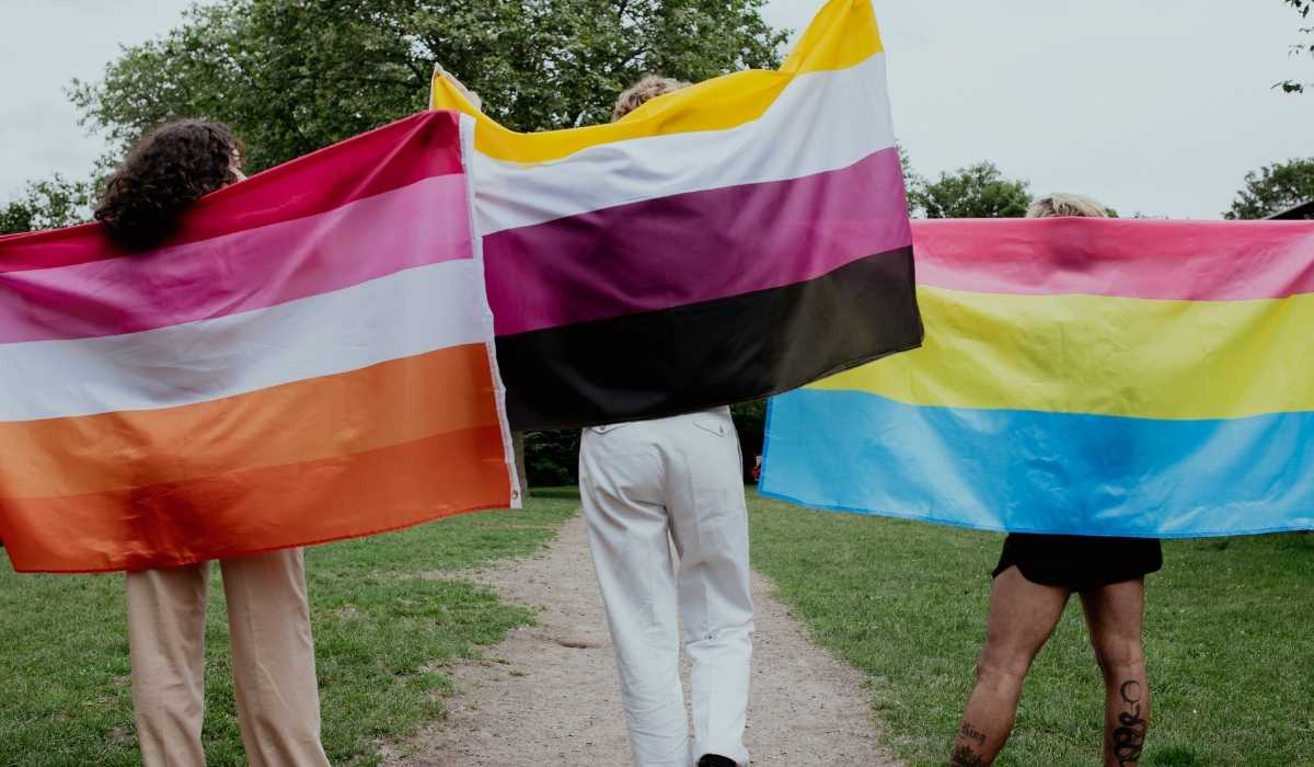 Three women holding rainbow flags on a path.