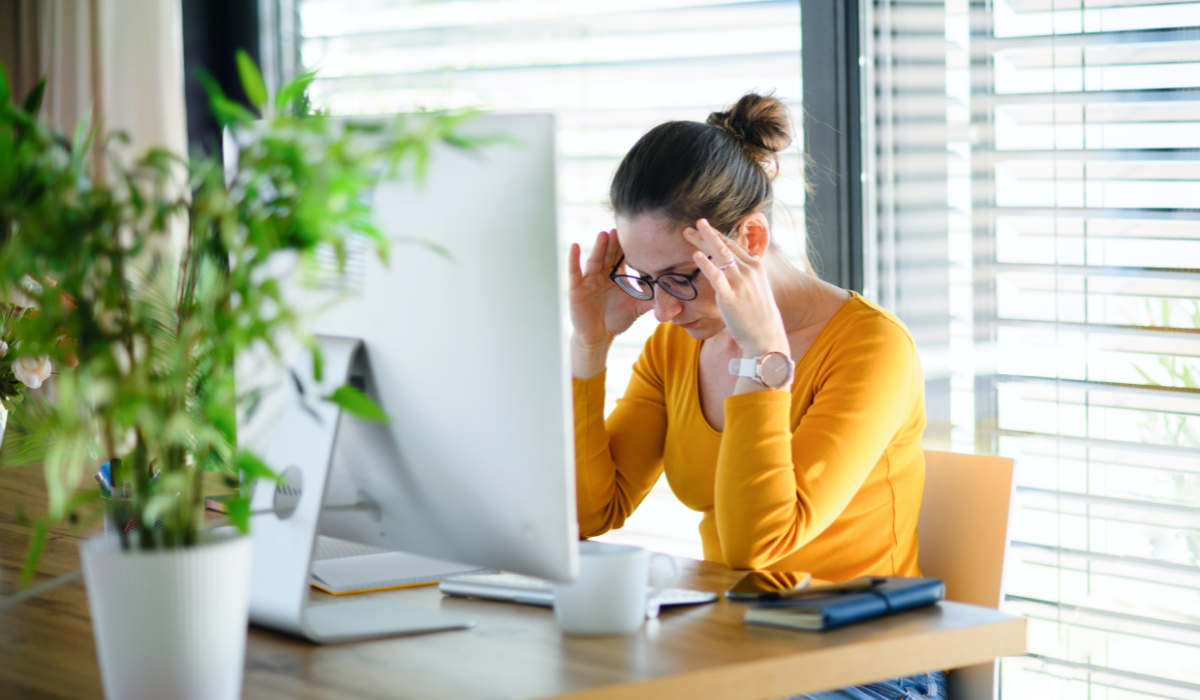 A woman is sitting at a desk with her hands on her head.