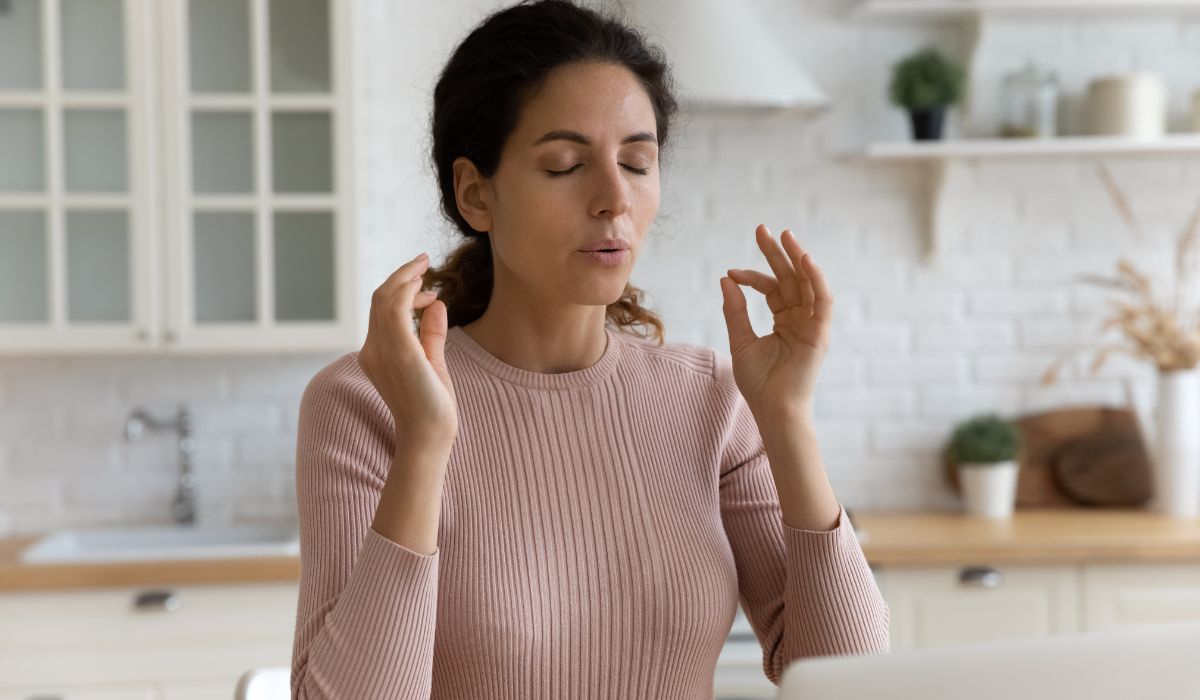 Woman meditating to relieve stress in a kitchen setting.