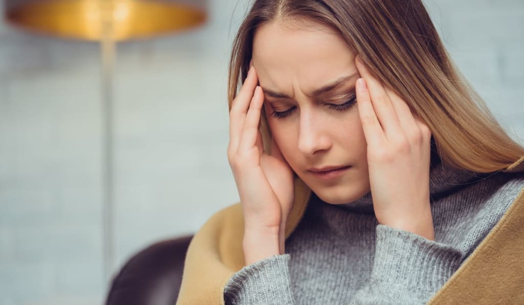 A woman sitting with her hands on her temples, eyes closed, appearing to have a headache or be in discomfort, possibly experiencing EMDR side effects.