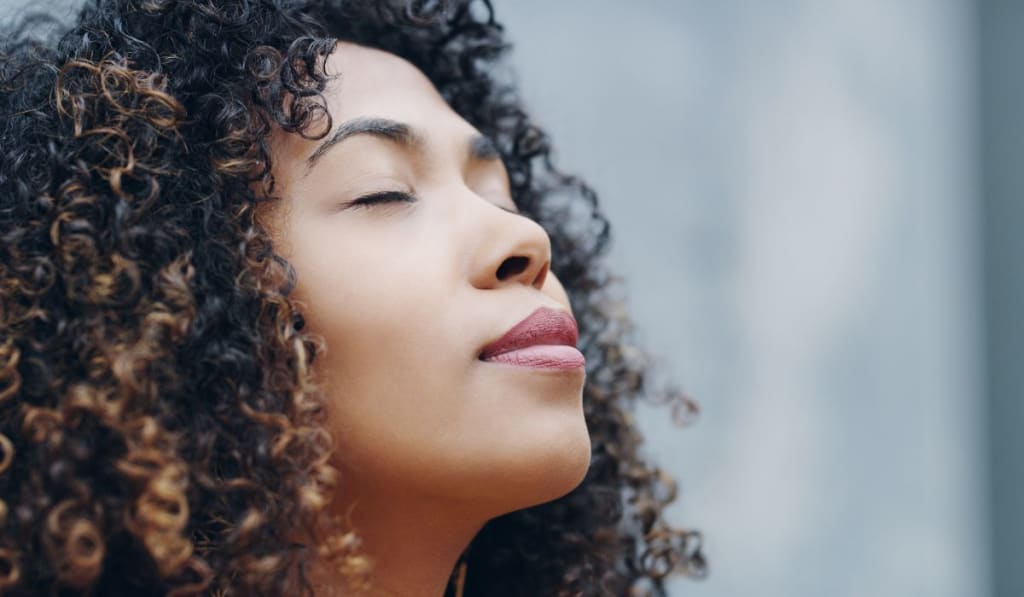 A woman with curly hair, eyes closed, and a peaceful expression seems to be enjoying a moment of serenity.
