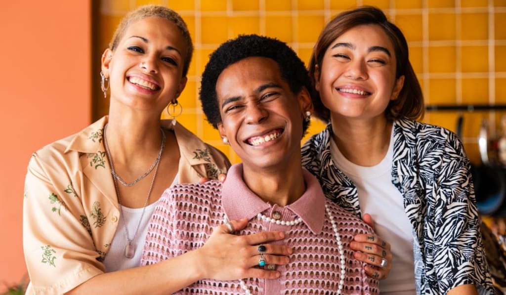 Three people smiling and posing together indoors in front of a tiled wall.