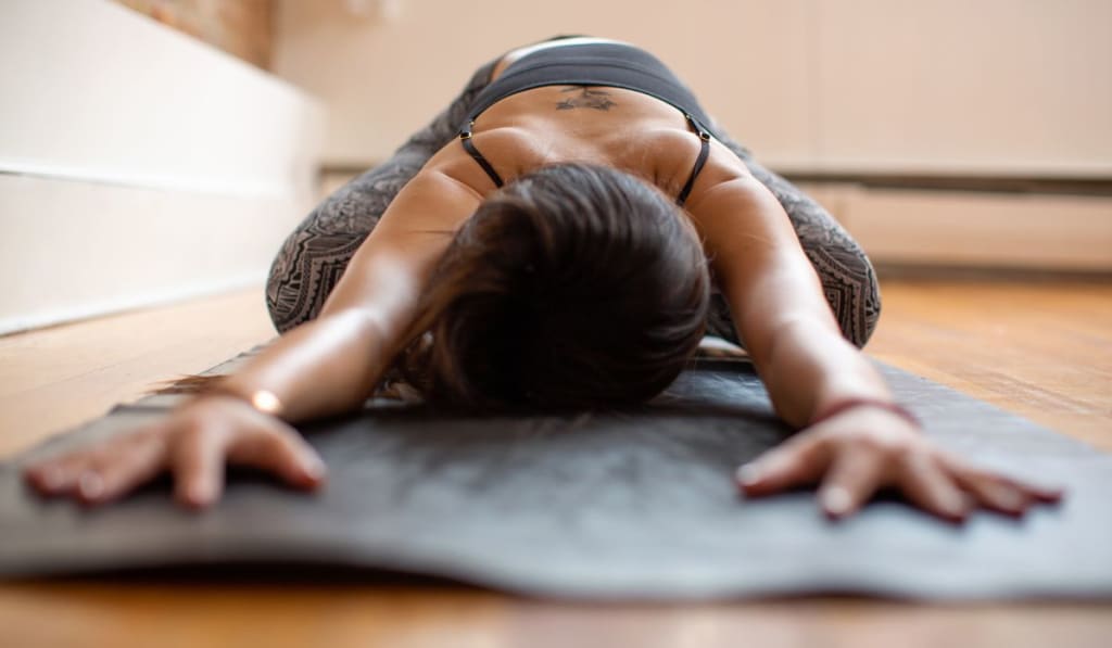 Person practicing yoga on a mat indoors, stretching forward with arms extended and forehead touching the mat.