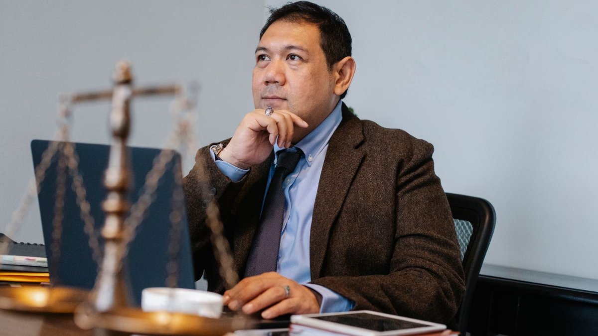 Website blocks access with 403 error Pensive Asian male lawyer in formal suit browsing netbook while sitting at table with decorative scale of justice and touchin