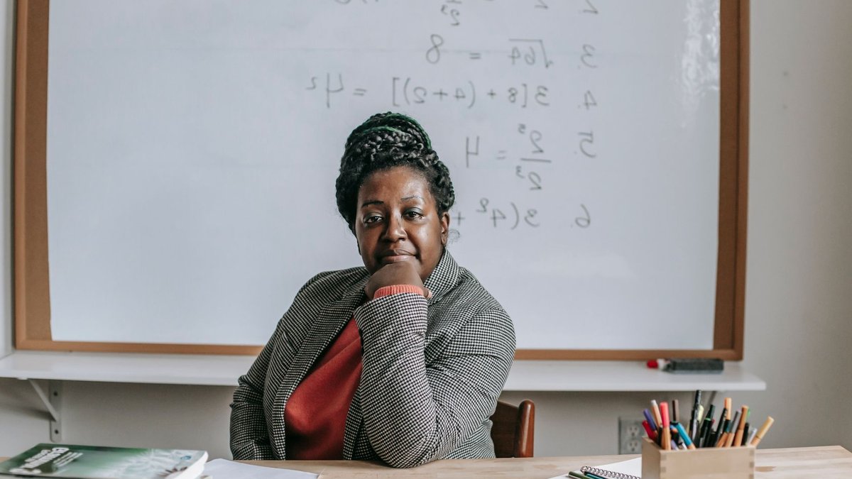Micro-Learning Strategies Drive Macro Professional Growth African American female teacher in formal clothes sitting at table with books and laptop and looking at camera.