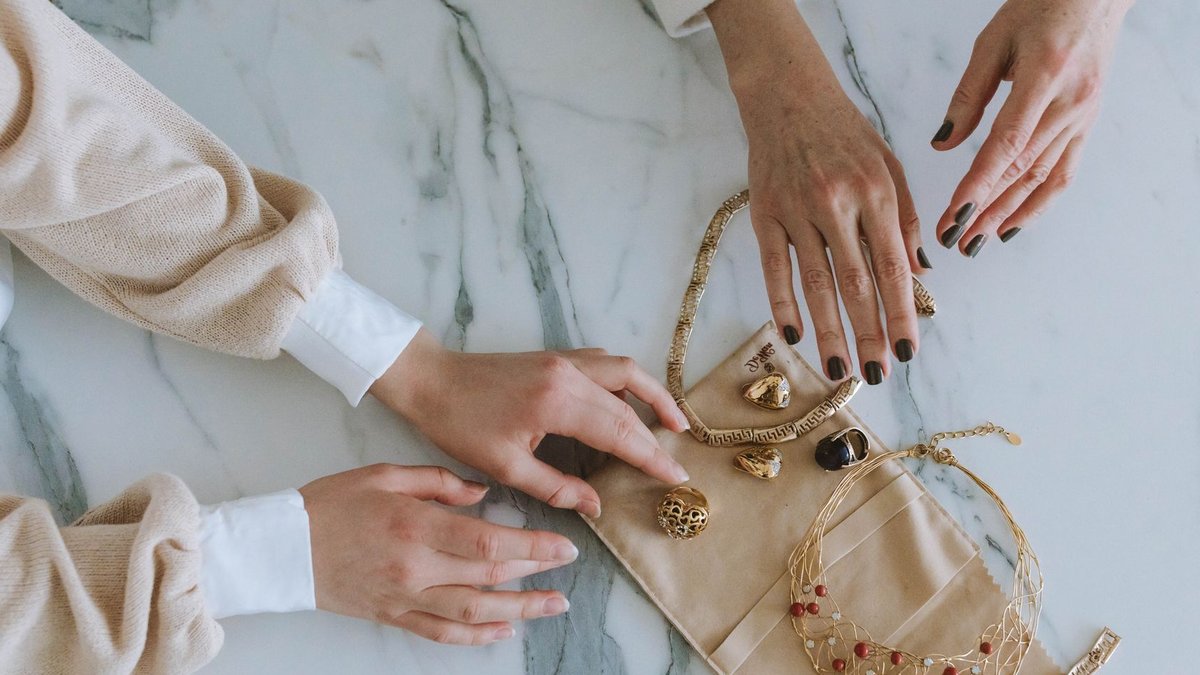 A sophisticated display of gold jewelry and hands on a marble surface, exuding luxury and elegance.
