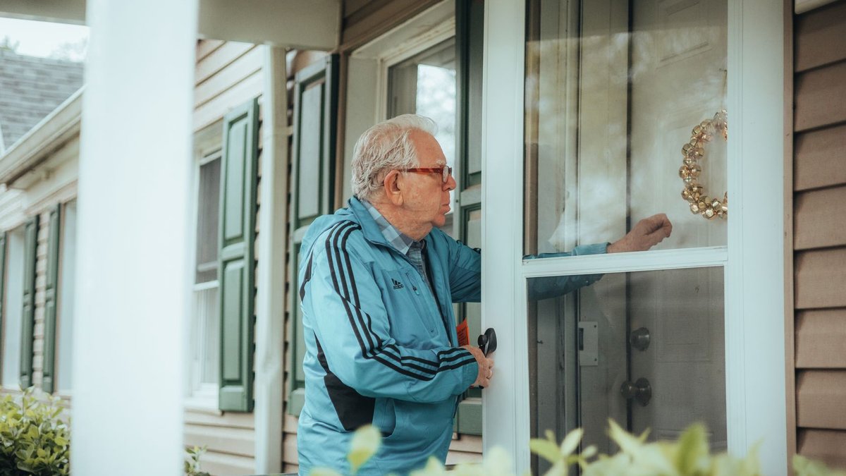 Elderly man in a blue jacket knocking on a suburban house door, showcasing community life.